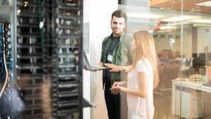 Dvoje ljudi u serverskoj sali razgovara nad laptopom o hosting nalozima
