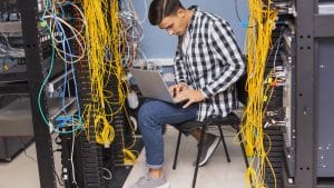 Inženjer sa laptopom u server sali dok proverava mrežnu opremu pri prenosu sajtova