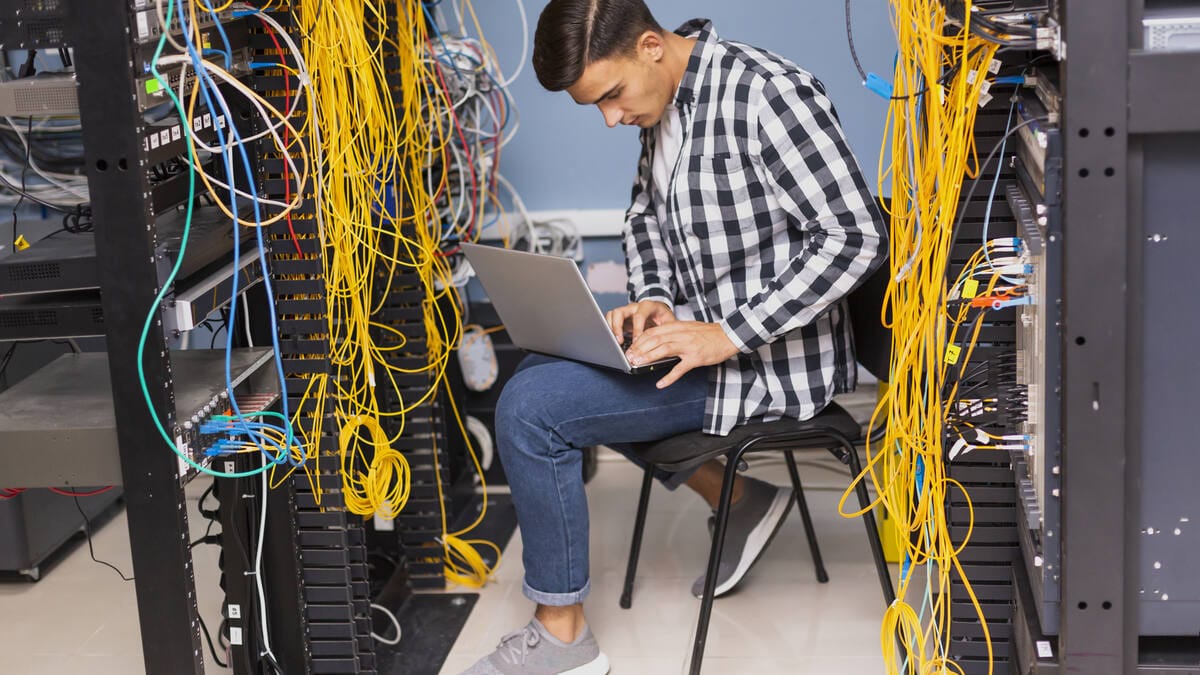 Inženjer sa laptopom u server sali dok proverava mrežnu opremu pri prenosu sajtova